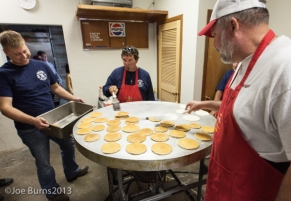 Man with pand waits for pancakes. Two men flip pancakes on griddle